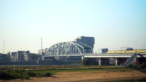 train crossing a bridge over a river in a city landscape.