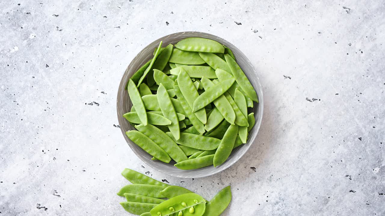 Fresh green peas in white ceramic bowl on gray stone background