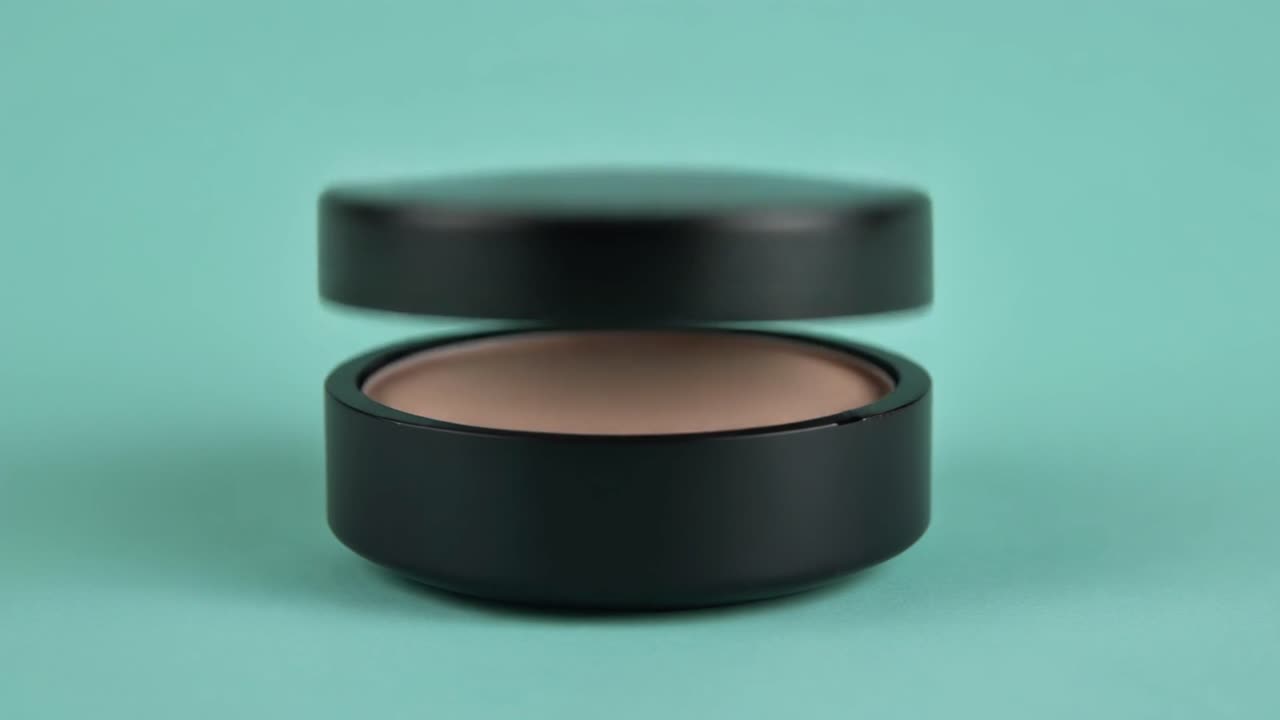 Black Cosmetic Jar Lid Being Placed on Teal Background