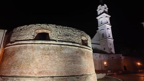 nighttime view of the rondella, a historic monument in sopron, hungary. the brick structure is beautifully illuminated against the dark sky, with the church tower standing tall in the background.