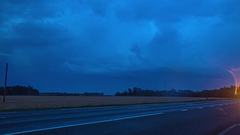 Tiro-De-Lapso-De-Tiempo-De-Los-Coches-Que-Conducen-A-Lo-Largo-De-La-Carretera-Rural-Con-Relámpagos-En-Las-Nubes-Oscuras-A-Lo-Largo-Del-Fondo-Durante-La-Noche