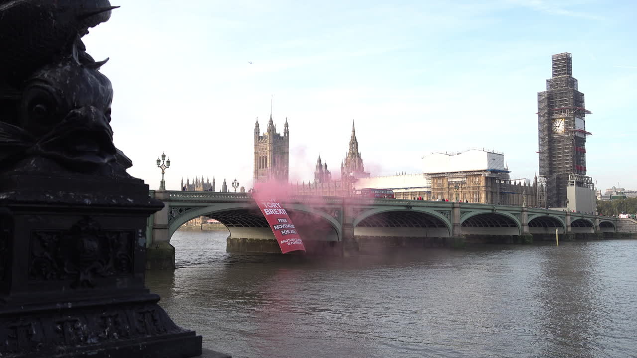 UK October 2018 - Another Europe is Possible campaign group protestors hang a large red banner from Westminster Bridge that says, “Stop Tory Brexit, Free Movement For All” and light red smoke flares.