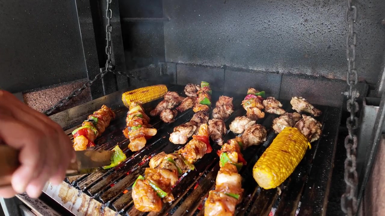 Spiedini di carne e mais alla griglia su un barbecue a carbone.