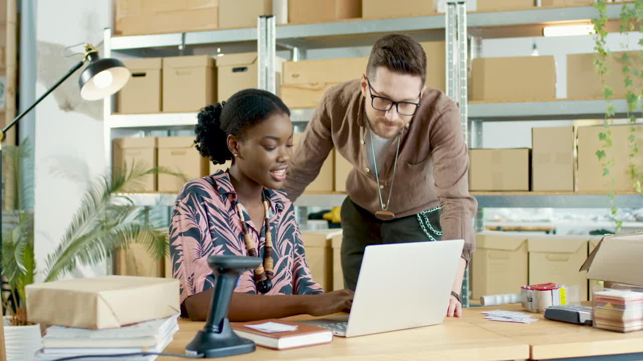 diseñadoras caucásicas y afroamericanas hablando mientras navegan en línea buscando en internet en una laptop en una tienda de ropa de moda