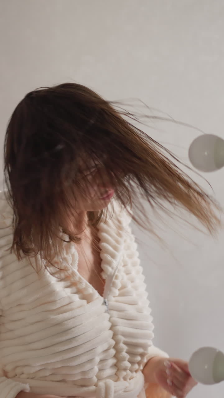 화장실에서 샤워를 한 후 머리를 흔들며 춤을 추는 여성. 로브를 입은 긍정적 인 여성은 램프와 함께 조명 된 화장실에 은 날아가는 머리카락을 회전시니다. 느린 동작