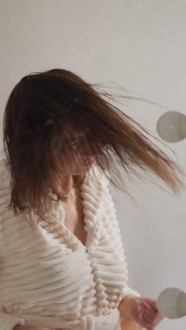 mujer sacude la cabeza bailando después de tomar una ducha en el baño. mujer positiva en túnica gira el cabello mojado volando en el inodoro iluminado con lámparas en cámara lenta
