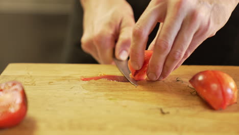 El-Chef-Corta-Cuidadosamente-Una-Cáscara-De-Tomate-Con-Un-Cuchillo-Sobre-Una-Tabla-De-Madera-Con-Las-Manos-Limpias,-Demostrando-Precisión-E-Higiene.