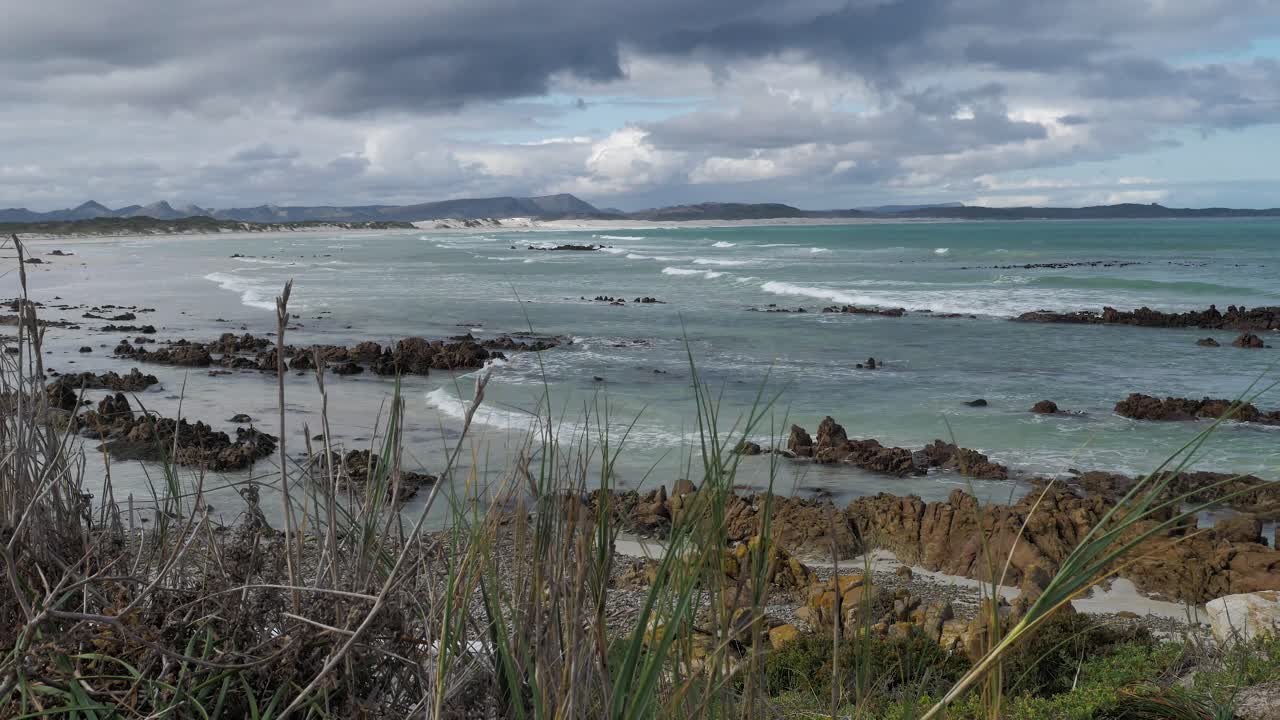 Onde che si infrangono su una spiaggia rocciosa con cieli tempestosi e drammatici, inquadratura panoramica