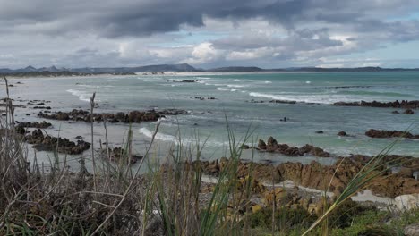 Waves-running-out-onto-rocky-beach-with-dramatic-stormy-skies,-panning-shot