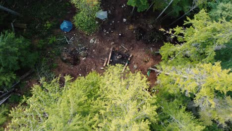 Ascending-drone-shot-of-camper-cooking-over-a-fire-in-the-woods-with-tents-in-the-background