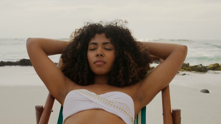 Vista frontale di donna afroamericana che dorme su una sdraio sulla spiaggia 4k