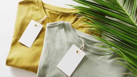 video of close up of folded green and mustard t shirts with tags on white background