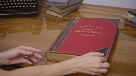 a shot of a big old book on the table, with some other smaller old books on the side, woman's hands reach to the books and carefully opens it