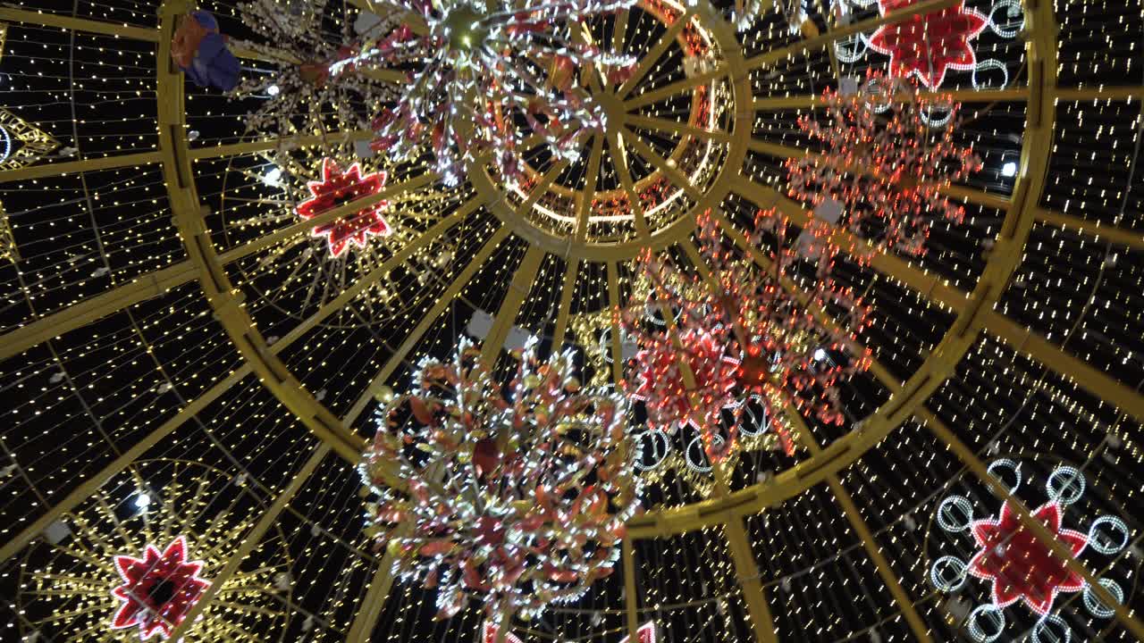 A big Christmas ball decorated with colorful sparkling lights patterned in different shapes and designs - Pan up shot