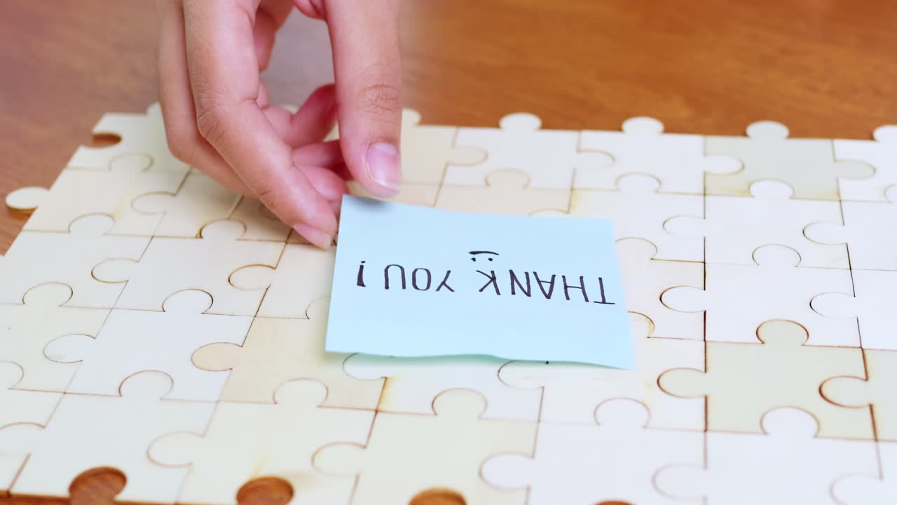 A hand places a thank-you note a completed puzzle symbolizing appreciation and joy