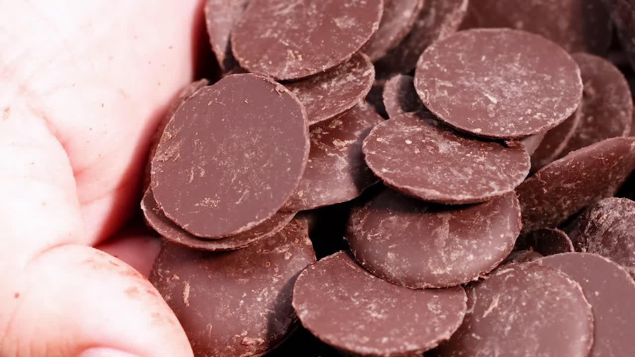 Detailed view of hands filled with smooth, round chocolate discs, showcasing texture and abundance.