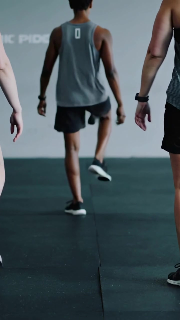 Vertical video: Leader starting high-knee march in gym wearing grey top and black shorts as warmup