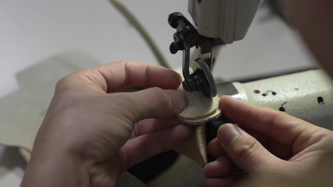 Artisan feeding a rolled suede strip through a sewing machine to bind a glove edge