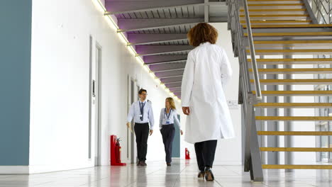 Two-Doctors-In-Discussion-As-They-Walk-Along-Hospital-Corridor