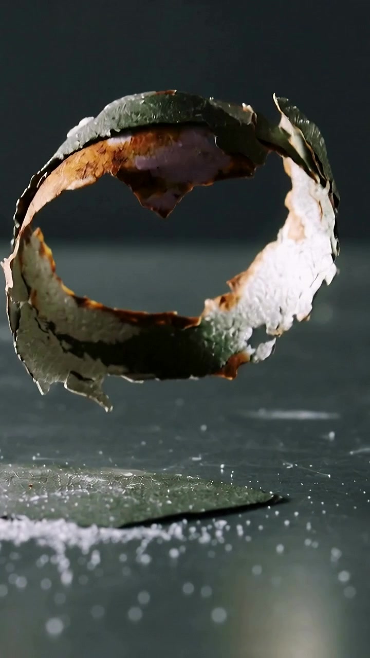 Vertical video: Dropping ring fragment from beam rotating onto studio table, scattering granules