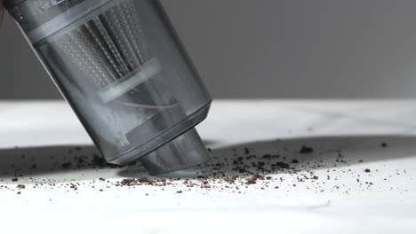 handheld vacuum cleaner removing coffee grounds from white surface