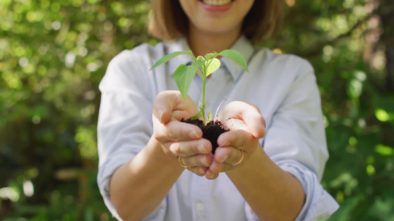 mujer asiática sosteniendo una planta en el jardín sonriendo en un día soleado