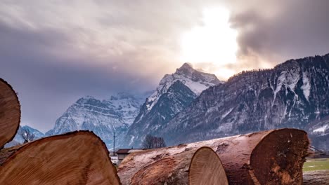 Gleitender-Zeitraffer-Hinter-Einem-Stapel-Baumstämme,-Um-Die-Wunderschöne-Berglandschaft-Der-Schweiz-Zu-Zeigen