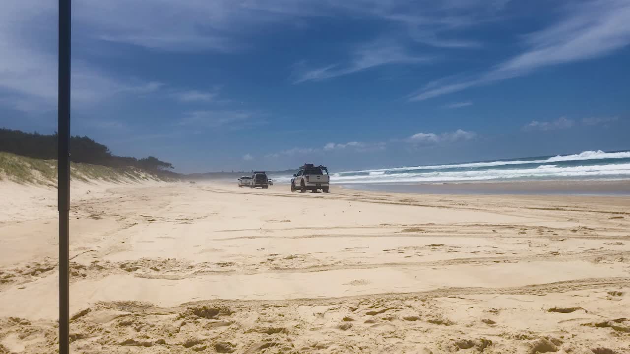 View north up Main Beach on Stradbroke Island, with 4x4 four wheel drive off-road trucks and cars driving up and down the beach on camping and fishing holiday in the Queensland hotspot