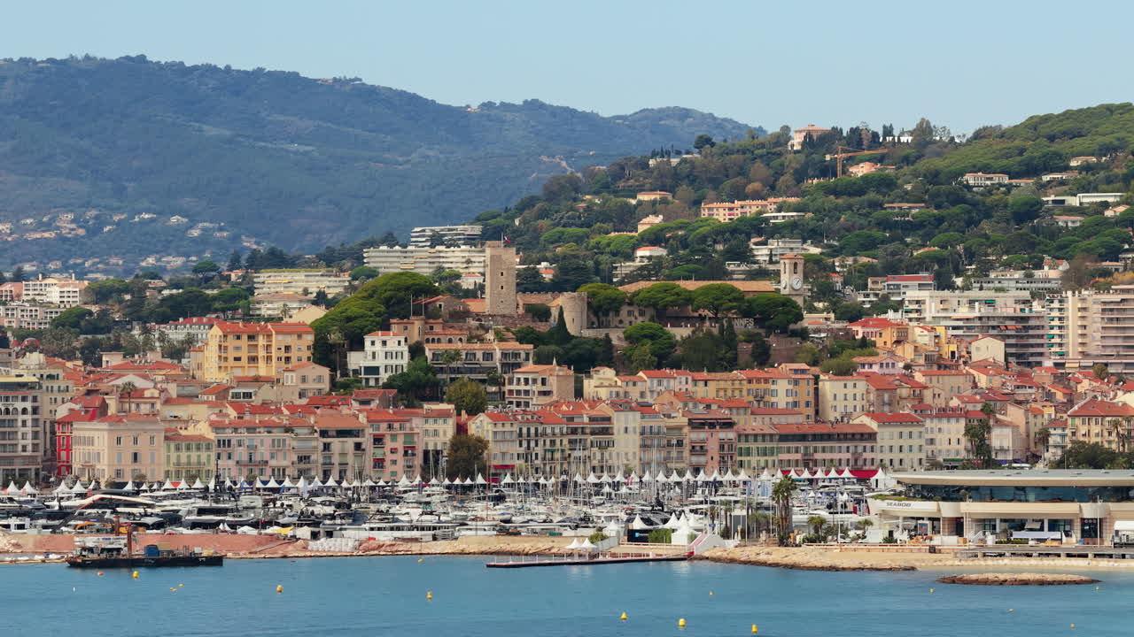 Aerial drone view of Cannes Old Town Le Suquet with historic tower, colorful rooftops, and luxury yachts in the marina