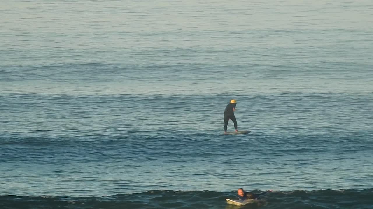 aerial view of a hydrofoil rider flying across the ocean, soaring above the waves with fluid precision. The water glistens as they glide effortlessly.