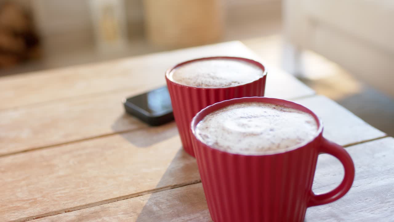 Lo spostamento della luce del giorno proietta riflessi su due tazze rosse di caffè schiumoso per enfatizzare l'atmosfera della cucina
