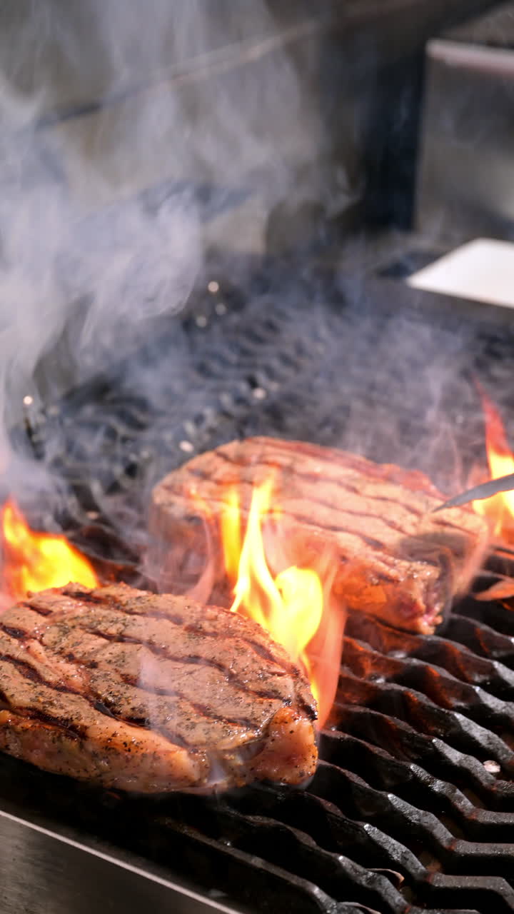 Juicy steaks grilling with flames. Two steaks with grill marks cooking over flames on a smoky grill