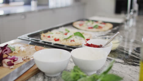 Close-up-of-olive-oil-in-bottles-and-pizza-on-baking-sheet-in-kitchen,-slow-motion