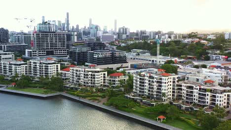 cinematic aerial view fly around newstead river terrace, waterfront residential apartment complex along brisbane river with downtown cityscape on the skyline at sunset, capital city of queensland