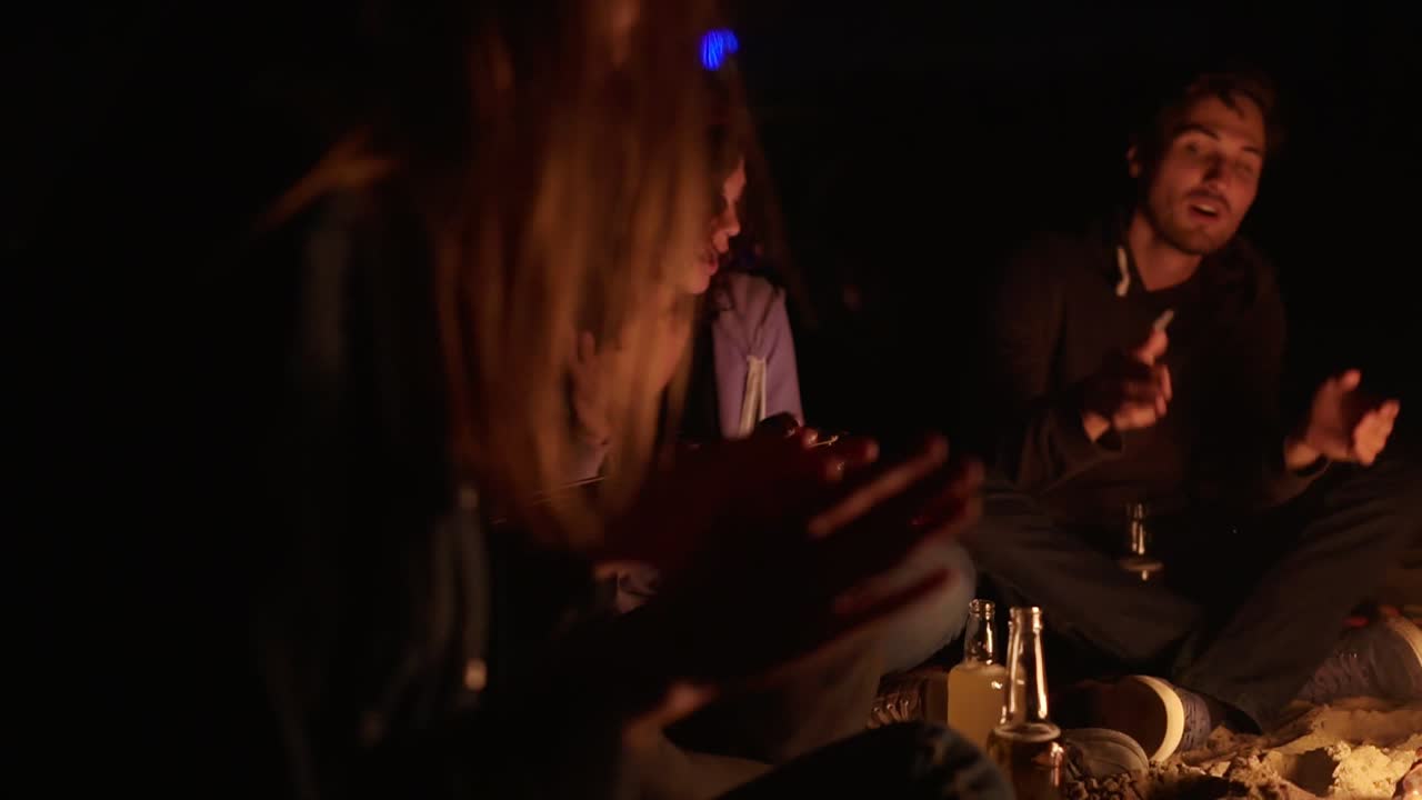 grupo multiétnico de jóvenes sentados junto a la hoguera tarde en la noche y cantando canciones y tocando la guitarra.