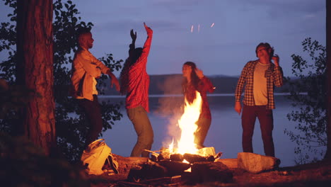 friends dancing around a campfire by the lake at night
