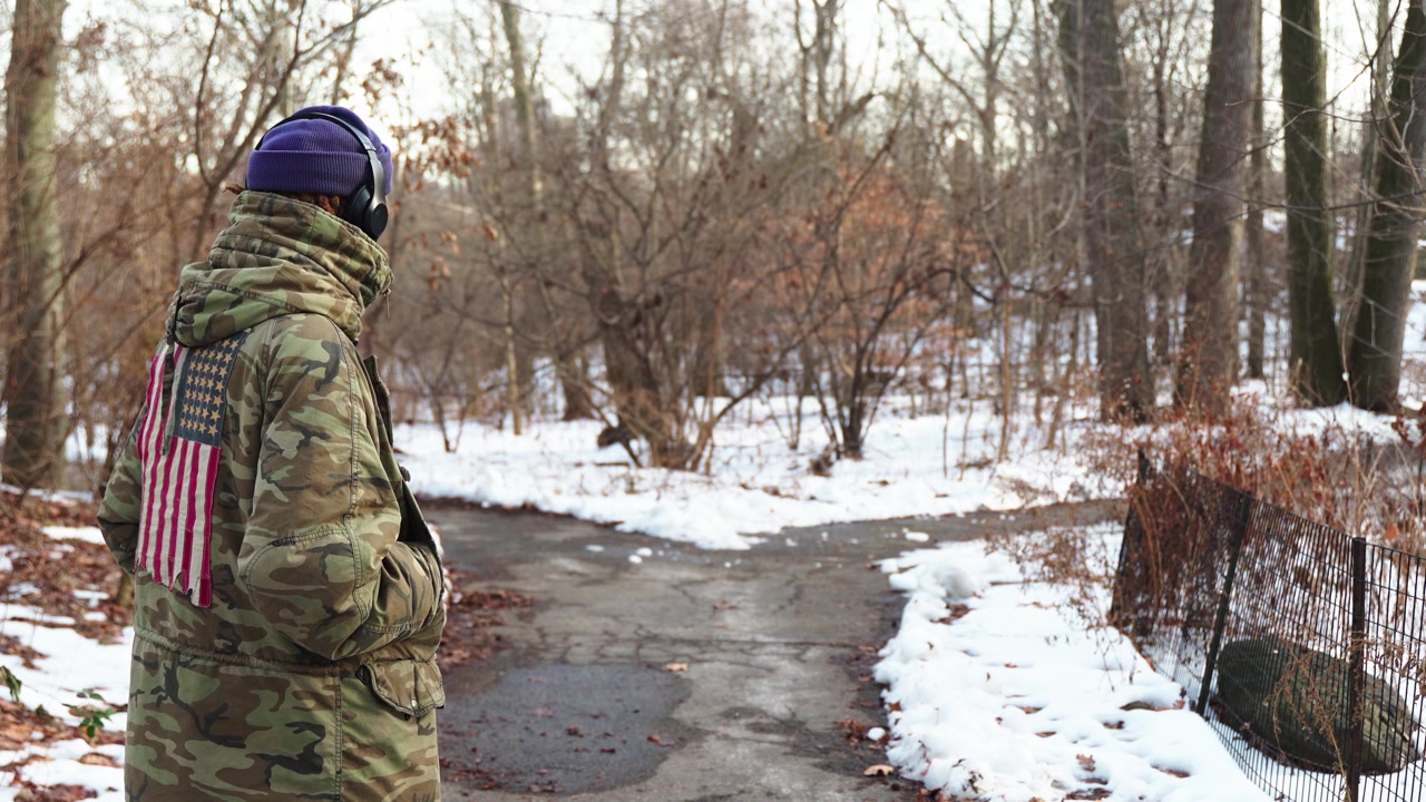 Un uomo afroamericano si trova di fronte a un paesaggio innevato, indossando un pesante cappotto invernale e un cappello con una sciarpa al collo. Trasmette un senso di pace e tranquillità