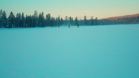 snowmobile riders driving across snowy lapland woodland towards camera at sunrise