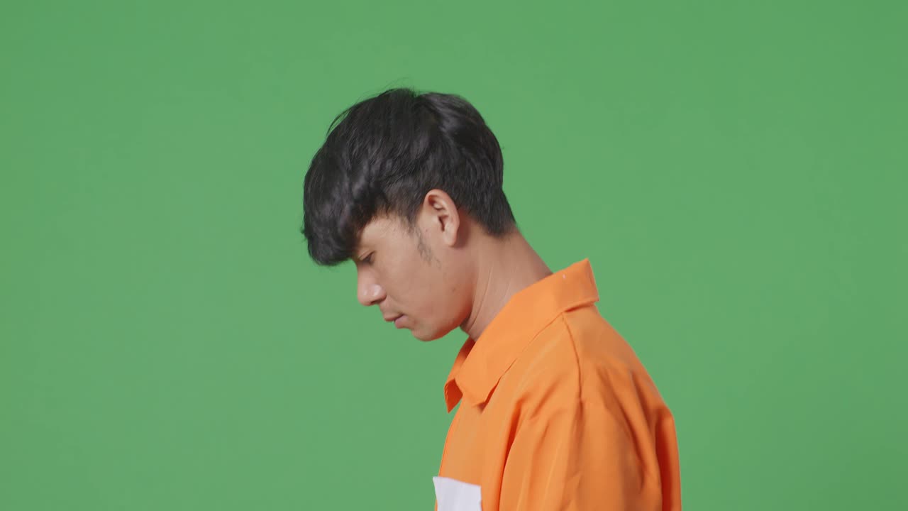 녹색 화면 배경에서 걸어다니는 수갑에 인 아시아 남성 죄수의 측면 뷰 클로즈업