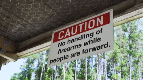 caution, no handling of firearms while people are forward signage on ceiling of firing range