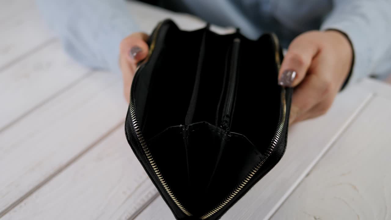 Close-up of a young woman opening an empty wallet on a light wooden background.