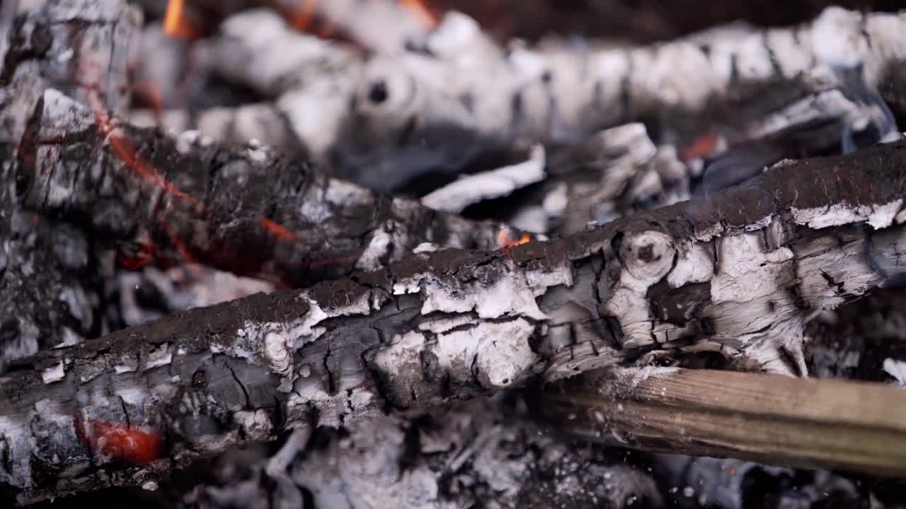 Motion of wooden logs in fire. Wooden stick turning over smoldered logs. Glowing firewood. Close-up.