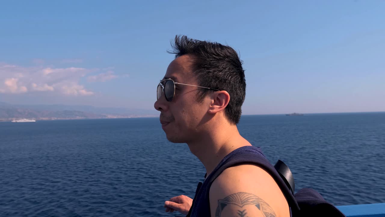 Slow Motion Stablized Circling Shot of Young Vietnamese Adult with Aviator Sunglasses Soaking in View of Sicily from Ferry