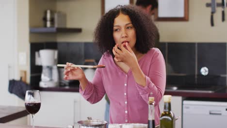 pareja feliz diversa preparando una comida juntos en la cocina, mujer probando comida y sonriendo