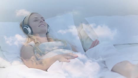 Animation-of-clouds-moving-over-caucasian-woman-with-eyes-closed-listening-music-while-lying-on-bed