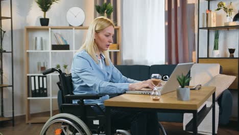 beautiful confident successful adult light-haired handicapped woman in wheelchair working on laptop in beautifully decorated home office,slow motion