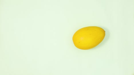 one yellow melon rotating on light green background. stop motion flay lay