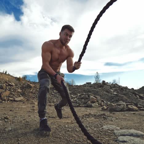 cross power training. concentrated sportsman exercises outdoors. young shirtless muscular man training with battle ropes on rocky background. slow motion