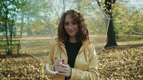 retrato de una mujer caucásica pelirroja con un paraguas transparente en el parque.