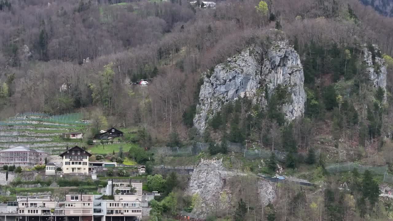 clip de avión no tripulado que muestra un helicóptero volando para dejar un paquete en una remota aldea alpina